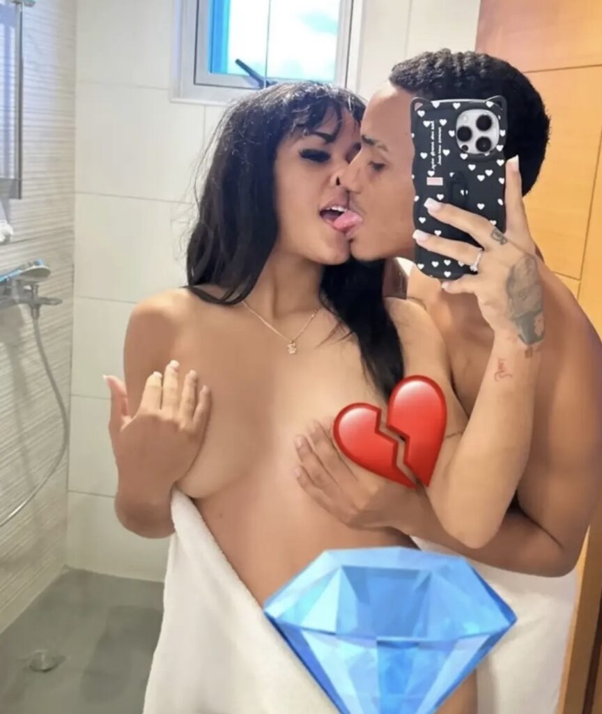 Young couple kissing in a bathroom mirror selfie; woman topless with a towel, man holding a phone with a heart-pattern case in view.